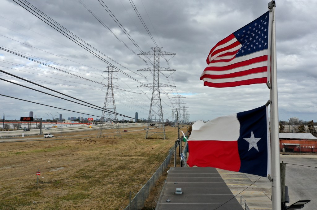 The U.S. and Texas flags fly in front of high voltage transmission towers on February 21, 2021 in Houston, Texas.