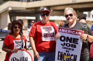 Three women who are in a union hold signs and wear shirts that say One Job Should Be Enough