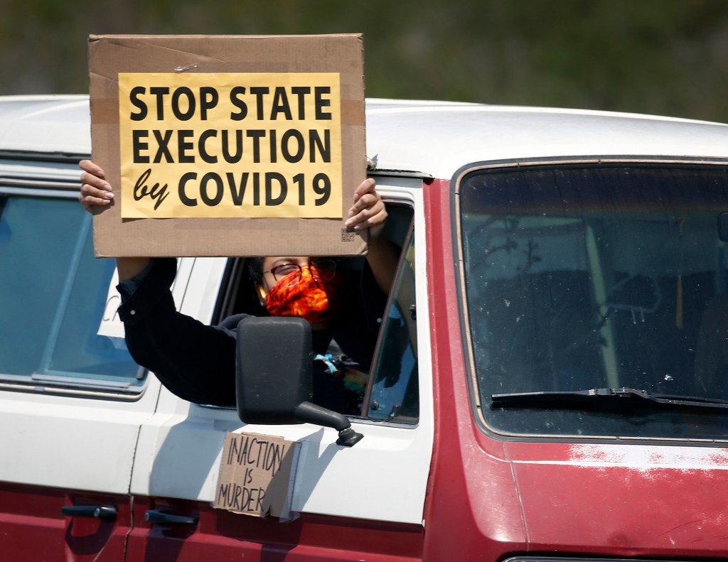 A woman displays a message demanding more protection for prisoners against the COVID-19, in Larkspur, Calif. on Saturday, May 9, 2020.