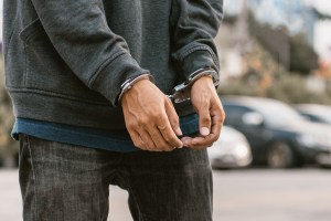 Under arrest, a man's hands with clenched fists are handcuffed behind him.