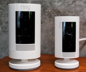 Two white Amazon Ring cameras sit on a brown wooden desk