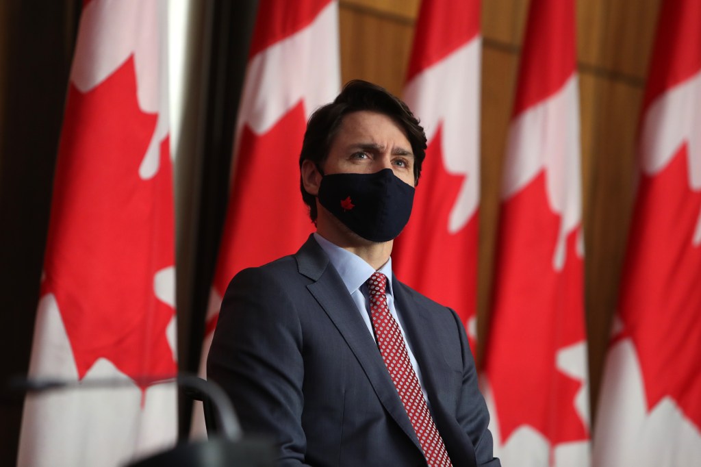 Prime Minister Justin Trudeau wearing a mask standing in front of Canadian flags at a press conference