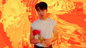 Jes Tom holding a red rose against an orange background