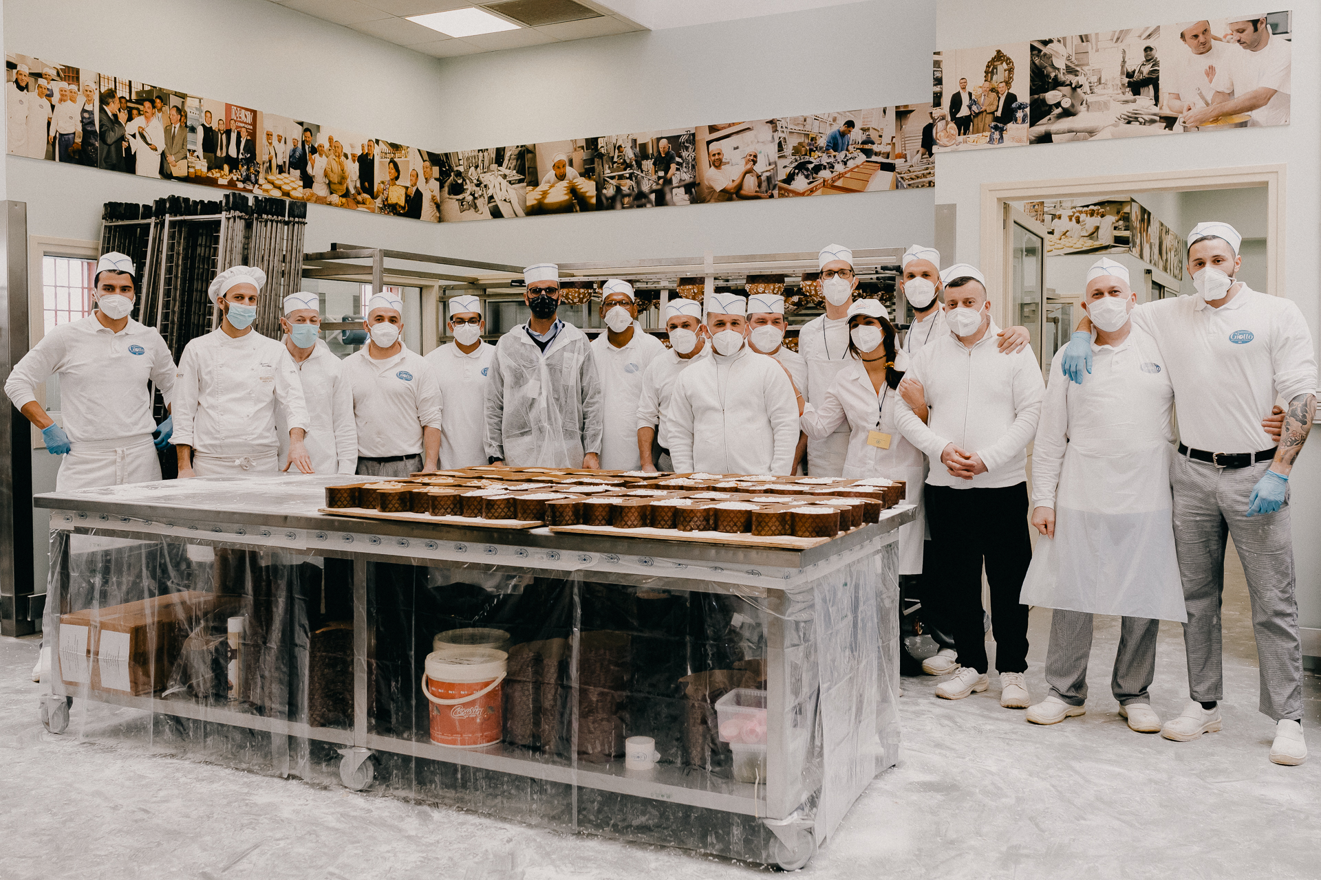 Giotto Bakery – A group picture of 15 men and one woman, standing side by side and hugging.