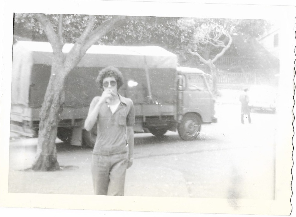 Mohammed Cheurfi – Mohammed Cheurfi – Photo of a man with an afro and aviator sunglasses, smoking a cigarette in front of a truck.