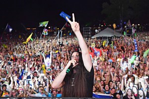 Bassnectar stands in front of a giant crowd making a peace sign