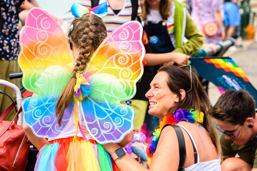 A young girl in rainbow butterfly costume with her mother during Brighton Pride Parade on Hove Lawns, Brighton, East Sussex, UK. 3rd August 2019.