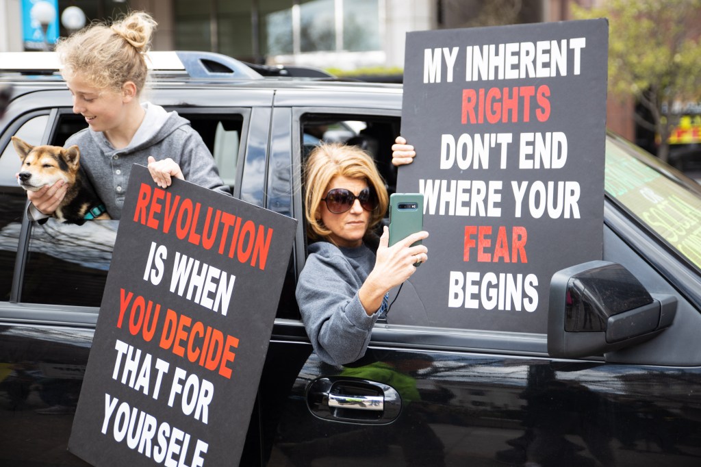 Photo shows a woman and a girl leaning out of a car window with anti-lockdown protest signs.