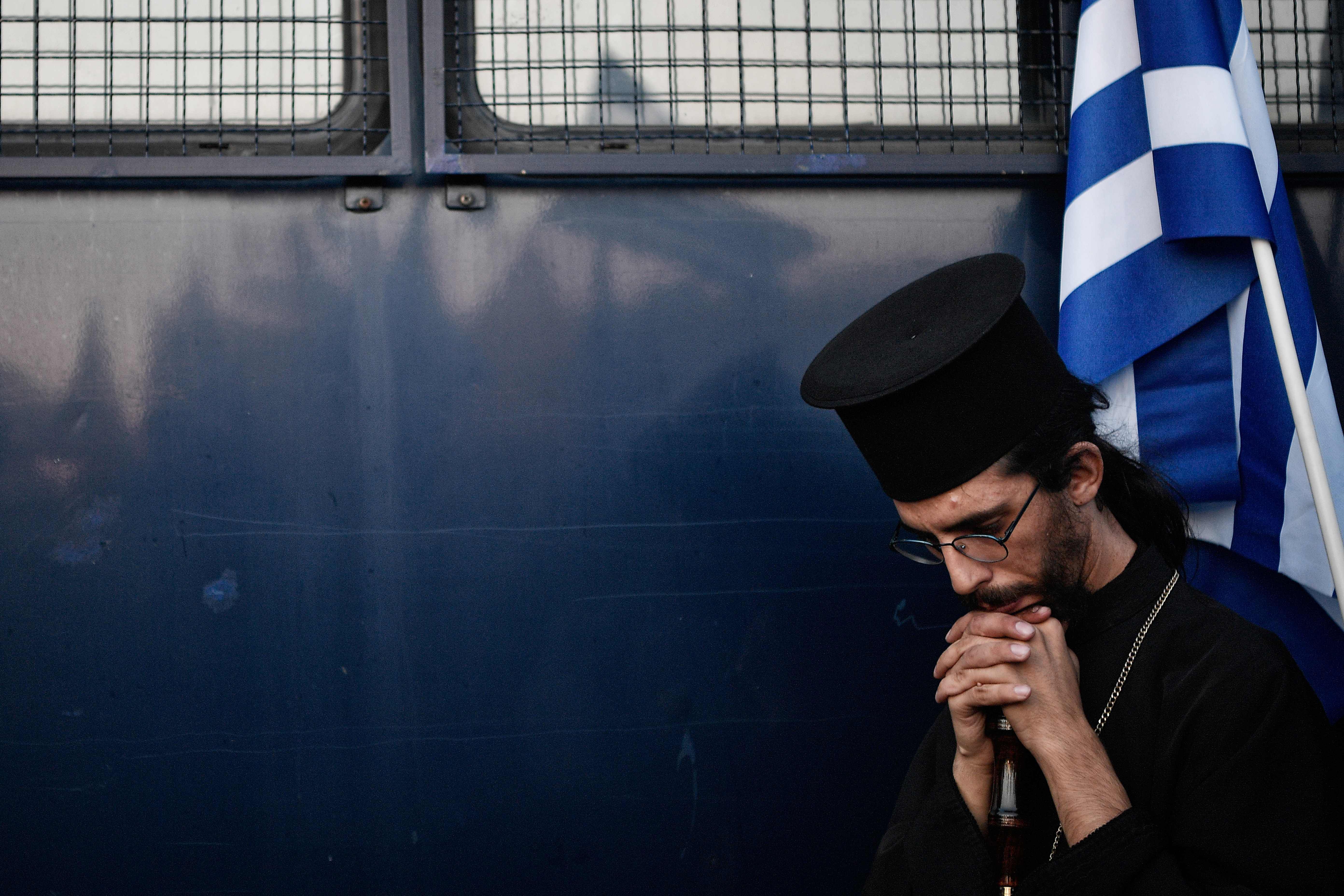 An orthodox priest stands by a police van during a Golden Dawn-led protest against the construction of a mosque in Athens. Photo: LOUISA GOULIAMAKI/AFP via Getty Images