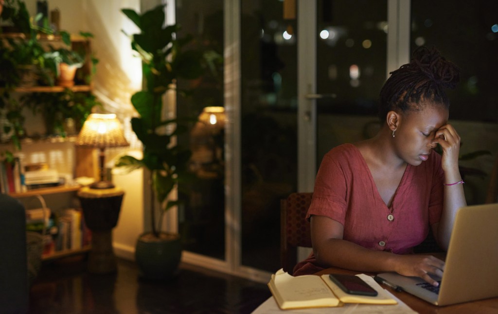 Een vrouw kijkt bedroefd terwijl ze 's avonds aan het werk is achter haar laptop