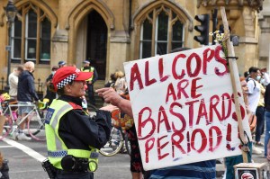 A police officer stands next to a banner reading All Cops are bastards period! at the a Black Trans Lives Matter march in the UK.