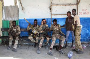 Six people in military fatigues sit on a bench in