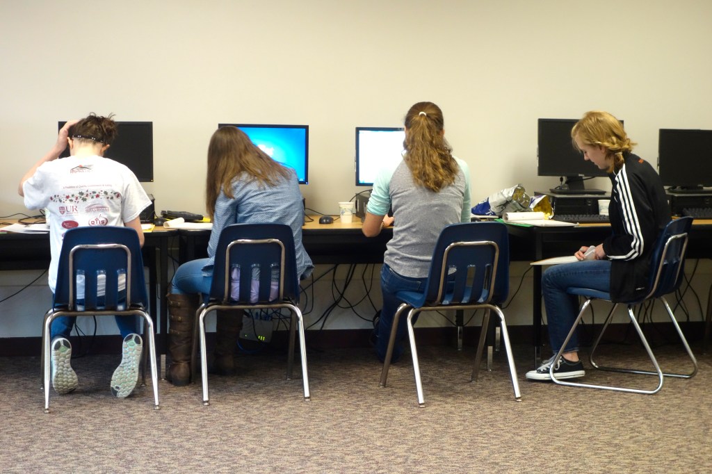 Students sit in blue chairs while working in a computer lab