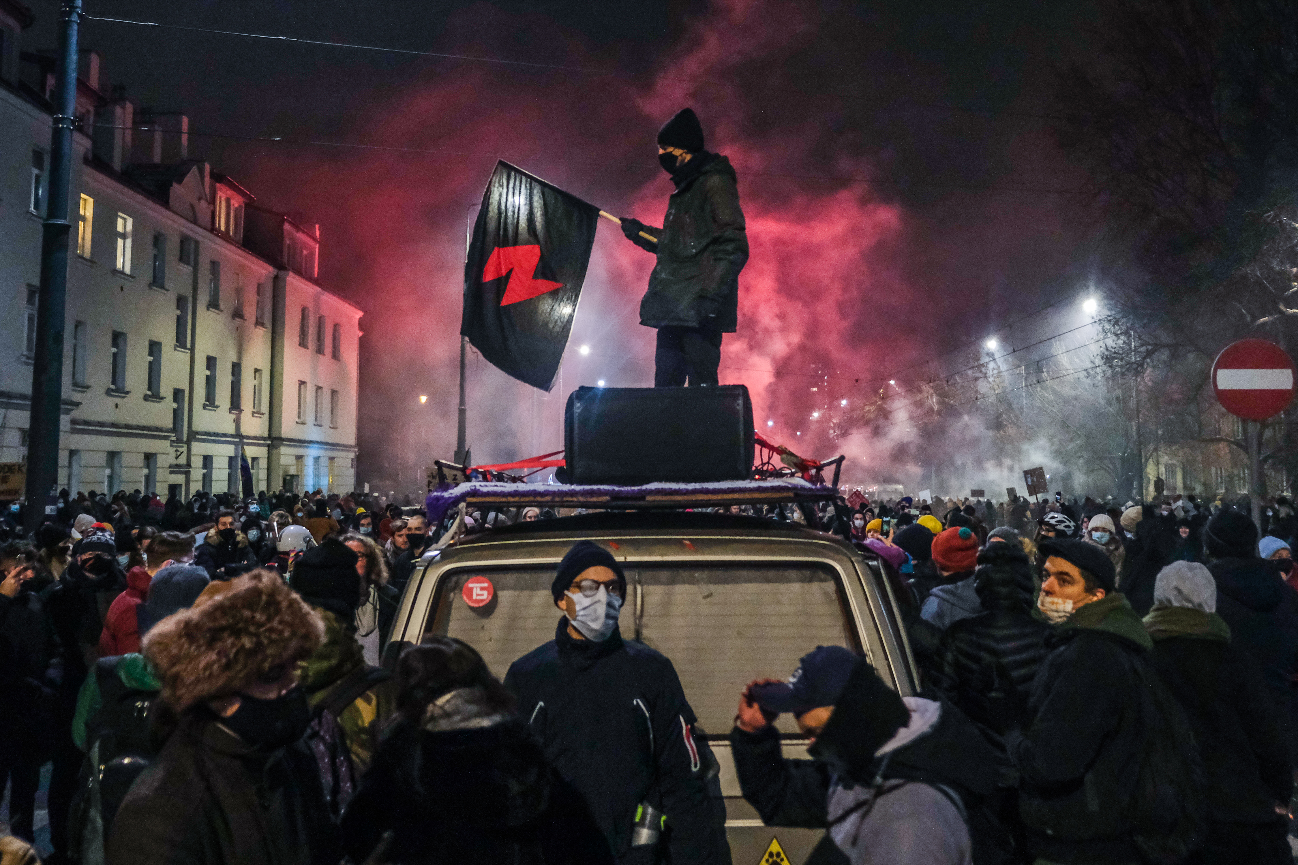 Ein schwarzgekleideter Mann steht inmitten einer Demonstration eine schwarz-rote Flagge haltend auf einem Auto über der Menge