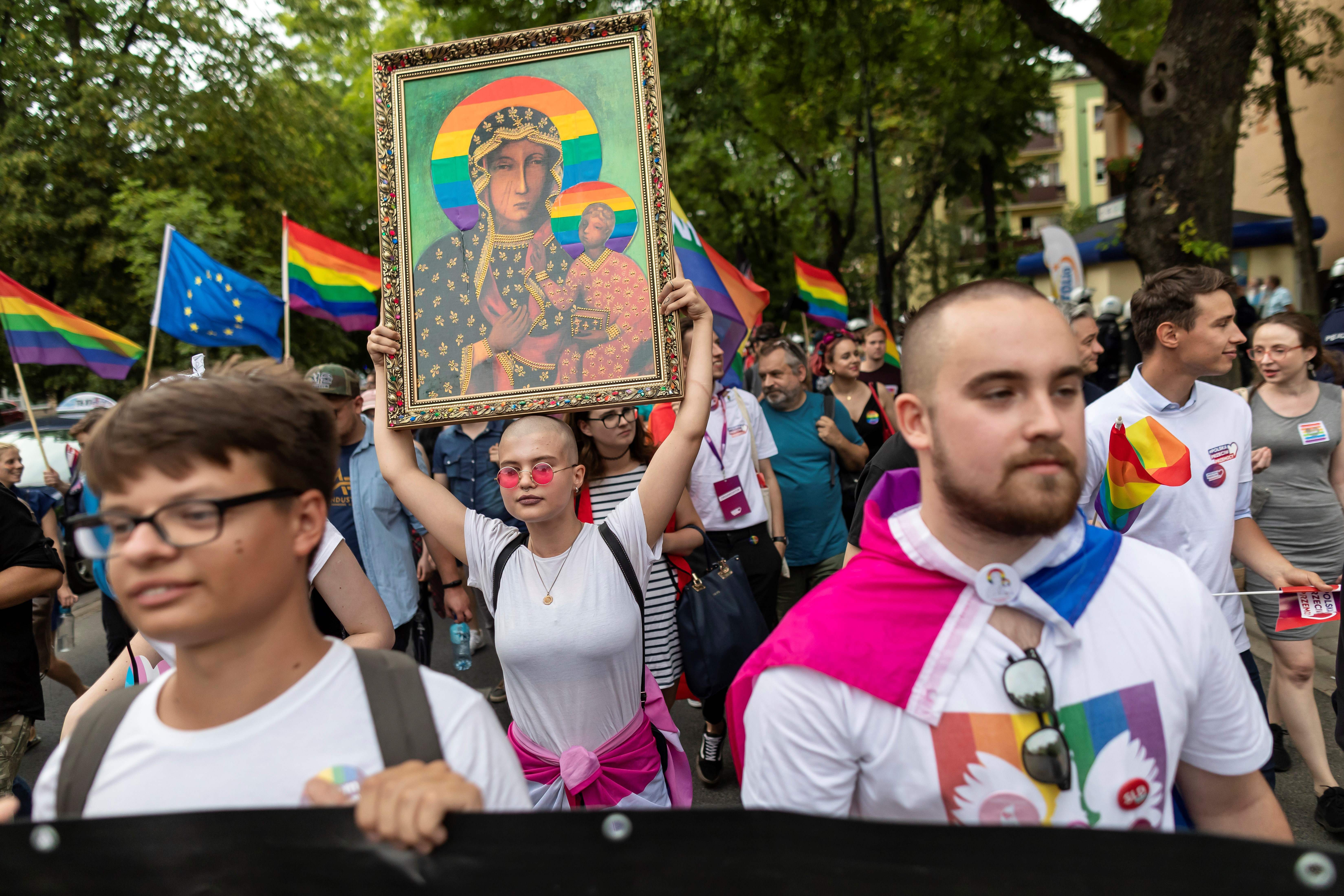 Demonstrierende mit weißen T-Shirts und Regenbogenflaggen, eine Frau hält eine Kirchenikone hoch, bei der die Heiligenscheine durch Regenbogen ersetzt wurden