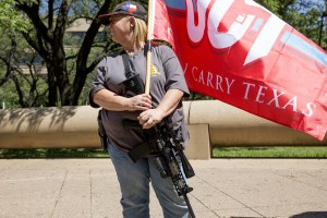 A demonstrator open-carries a rifle while holding a flag during a pro-gun rally on the sidelines of the National Rifle Association (NRA) annual meeting in Dallas, Texas, U.S., on Saturday, May 5, 2018.