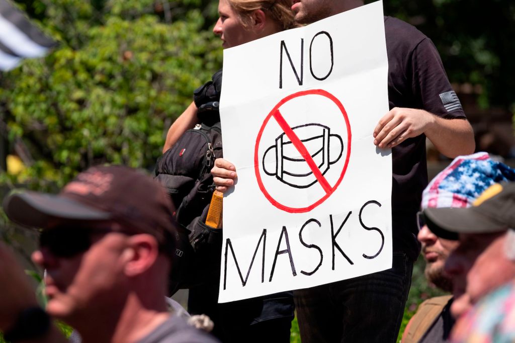 An anti-mask protester holds up a "no masks" sign.