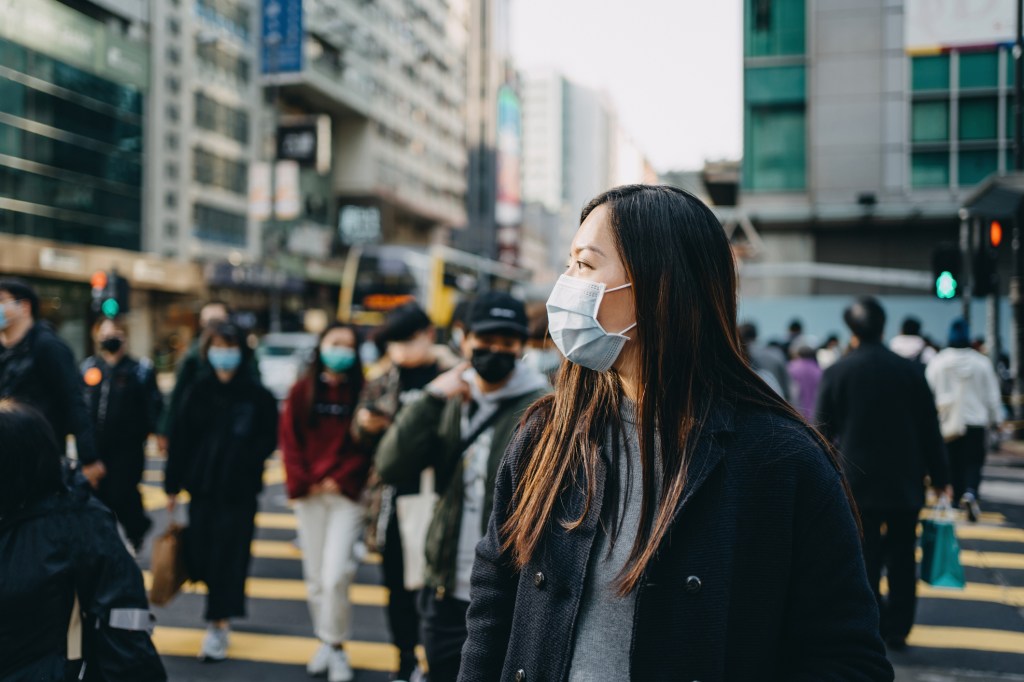 A woman wearing a mask walks down a busy street.