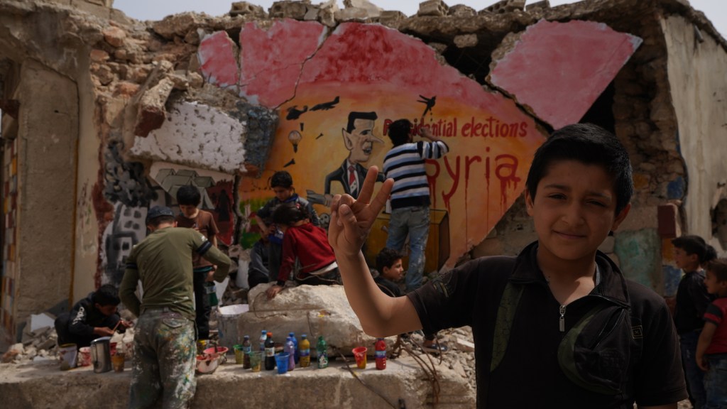 ​Children help Aziz Asmar graffiti a demolished wall.