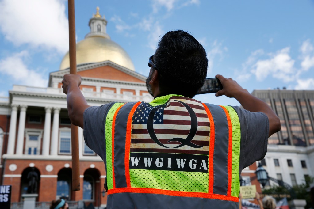 A man wearing a QAnon vest held a flag during a No Mandatory Flu Shot rally outside of the statehouse in Boston on Aug. 30, 2020.