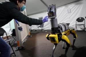 A man leans over to operate the touch screen of an iPad mounted on top of a yellow and black four-legged robot.