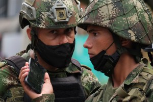 Soldiers listen to news on a mobile phone near the military base where a car bomb exploded in Cucuta, Colombia, Tuesday, June 15, 2021.