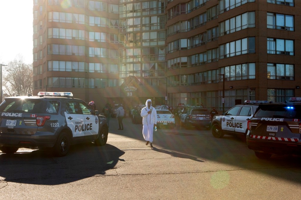 A resident of a building walks past parked police cars after officers arrived to enforce the eviction of a tenant, in Toronto on Friday, April 2, 2021​