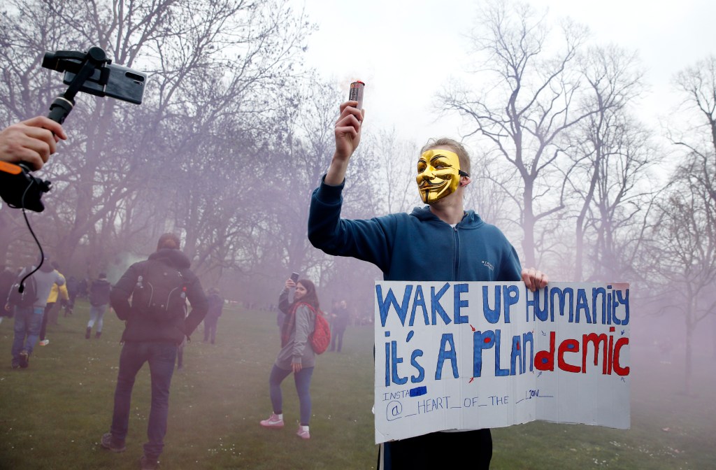 A protester with a flare poses holding a sign calling for people to "wake up" during a "World Wide Rally For Freedom" protest on March 20, 2021 in London, England.(Photo by Hollie Adams/Getty Images)