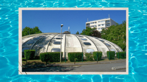 Piscine tournesol, sunflower pool – white dome with vertical rows of portholes surrounded by edges, a fence and a parking lot.