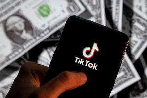 A close-up of a person looking at TikTok against a backdrop of dollar bills