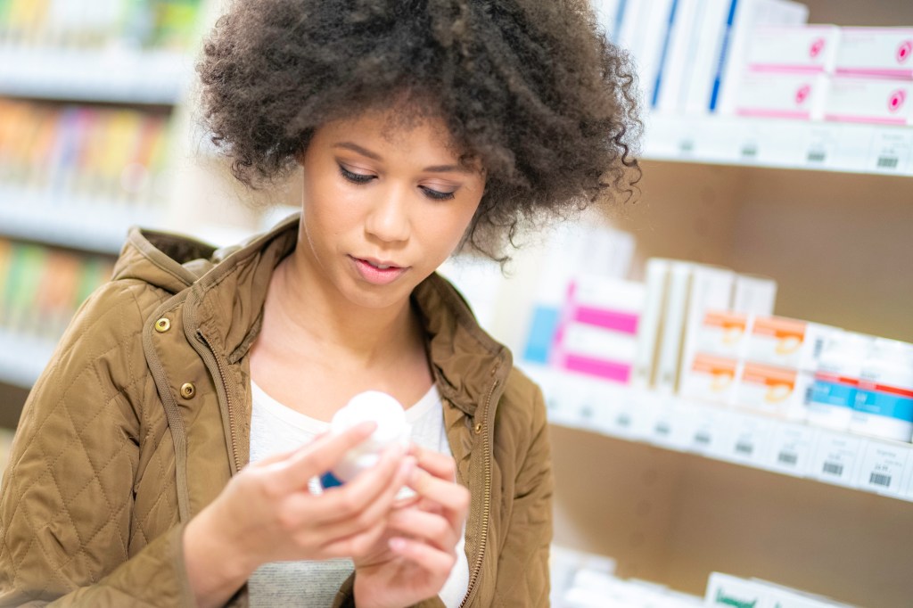 Close up front view of a Black woman in a drugstore reading instructions on a bottle of pills.