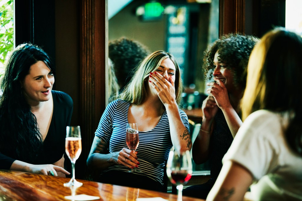 Laughing group of women enjoying drinks in bar - stock photo