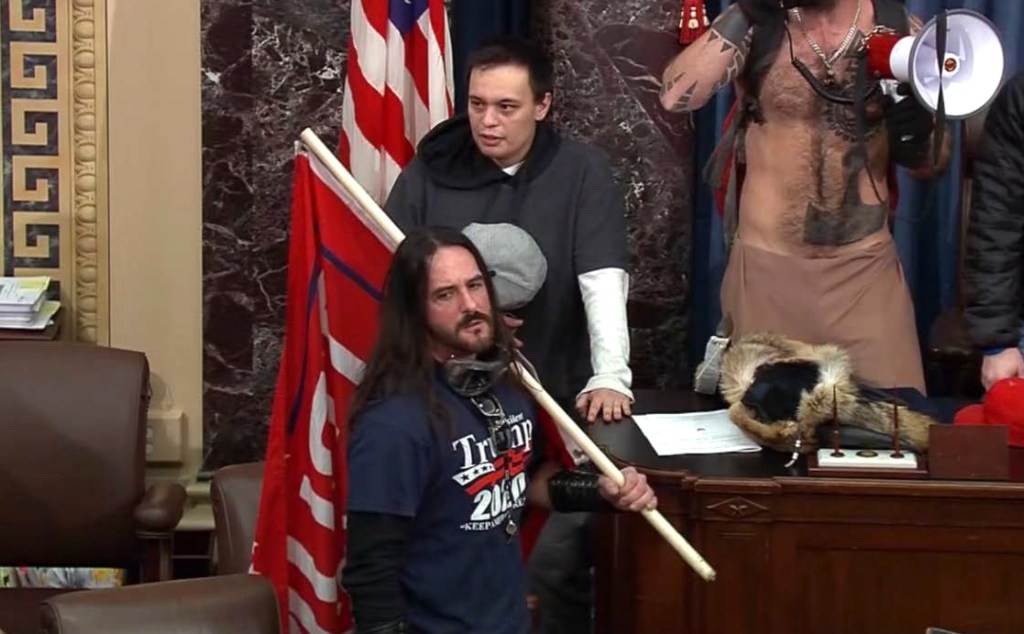 In this image from U.S. Capitol Police video, Paul Allard Hodgkins, 38, of Tampa, Fla., front, stands in the well on the floor of the U.S. Senate on Jan. 6, 2021, at the Capitol in Washington.