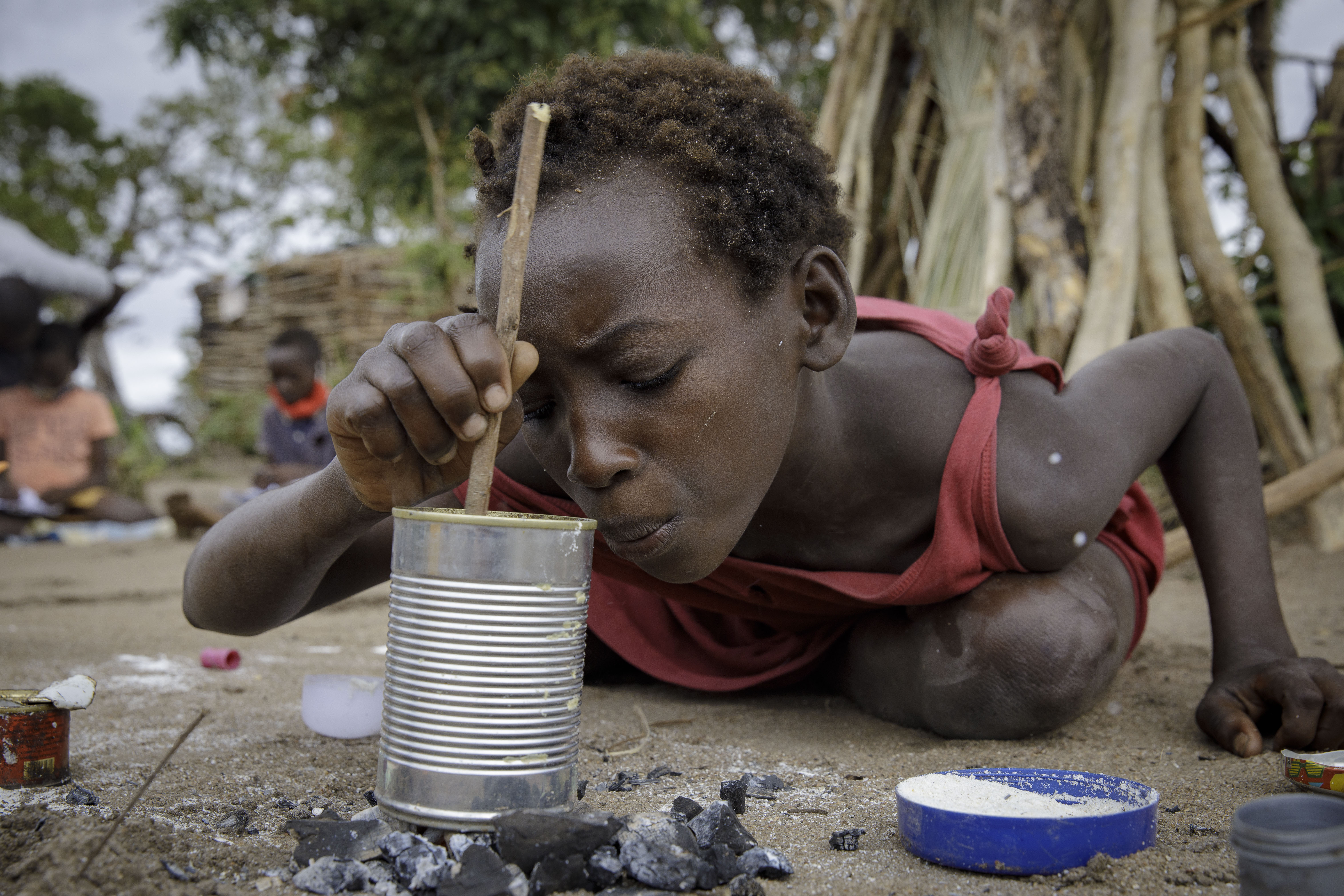 A girl cooks in a tin can in Mutua resettlement camp, Sofala province, central Mozambique