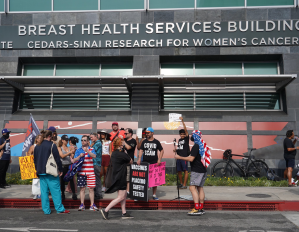 Dozens of anti-maskers holding signs with anti-vaxx and QAnon-adjacent conspiracy theories amassed on the sidewalk by the Cedars-Sinai Breast Health Services building on Thursday afternoon, and harassed patients and doctors.