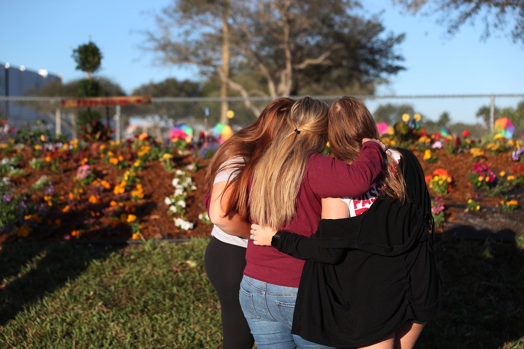 Two sisters hug their mother while looking on at a memorial setup for those killed at Marjory Stoneman Douglas High School on February 14, 2019 in Parkland, Florida. (Joe Raedle/Getty Images)​