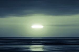 An unidentified flying object shines brightly over water.