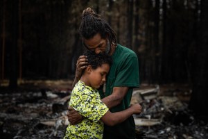 Nicolas Bey, 11, hugs his father, Sayyid, on the ground where their home once stood in Sycan Forest Estates, north of Bly, Oregon, on July 27, 2021. "As long as me and him are up here, even with this fire and everything burnt, I can still be happy with hi