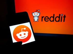 A hand holding a phone with the Reddit logo.