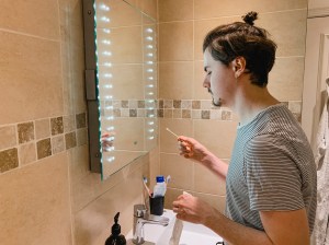 Caucasian man using a home test kit for coronavirus in his home. He is standing in front of a mirror in his bathroom holding a cotton swab.