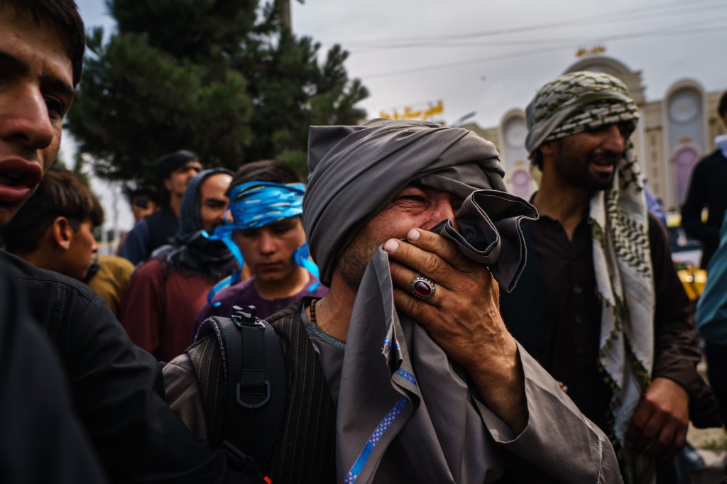 A man cries as he watches fellow Afghans get wounded after Taliban fighters use guns fire, whips, sticks and sharp objects to maintain crowd control over thousands of Afghans who continue to wait outside the Kabul Airport for a way out, on airport road in