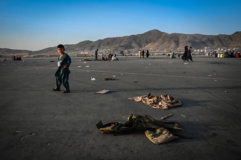 Niño afgano camina cerca de uniformes militares en el aeropuerto de Kabul