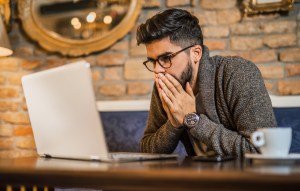 A man looks shocked at a laptop.