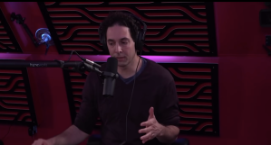 Image shows Alex Berenson wearing headphones speaking into a microphone.