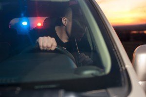 A man driving with police lights behind him.