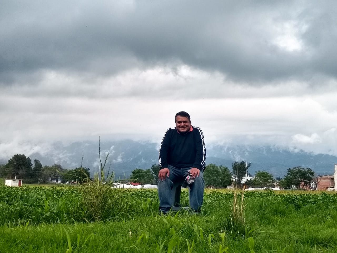 Dalila Anzueto, Viko Rodríguez, Mexico - A man in jeans and a dark sweatshirt shits in front of the cloud covered base of a volcano.