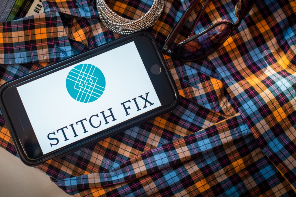 The Stitch Fix logo on a smartphone resting on top of clothes and jewelry styled together.