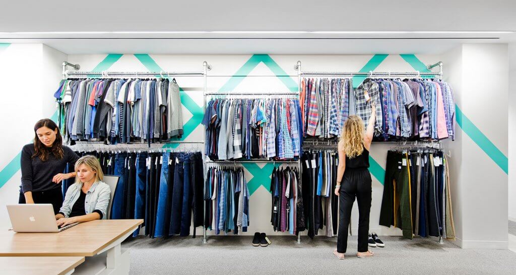 Women working in the Stitch Fix office in front of racks of clothing.