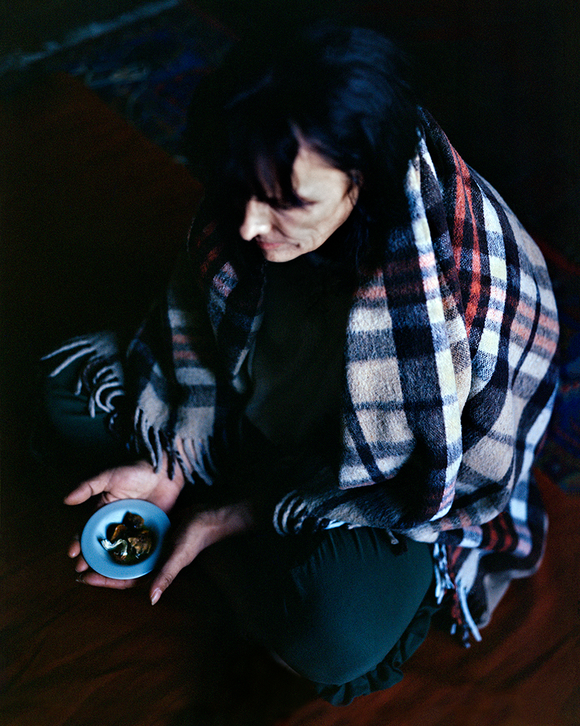 Mathias de Lattre, France, magic mushrooms - woman sat on floor wrapped in tartan shawl clutches small blue bowl in her lap