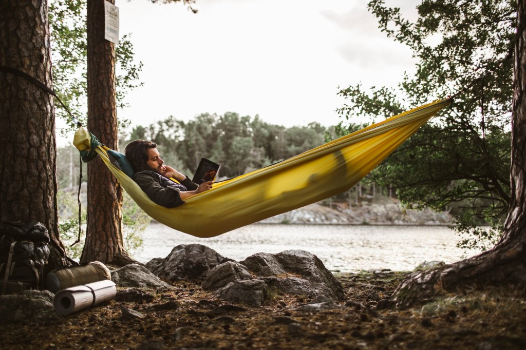 Man reads in a hammock by a lake.